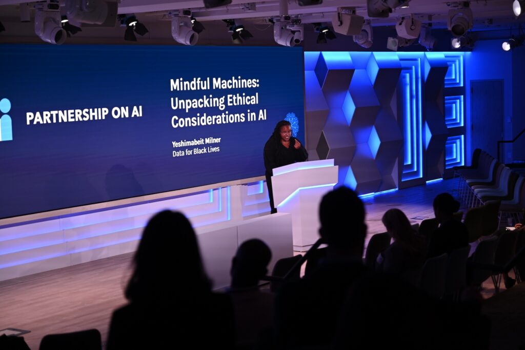 Yeshimabeit Milner on stage presenting a lightning talk at the AI & Philanthropy Forum in NYC